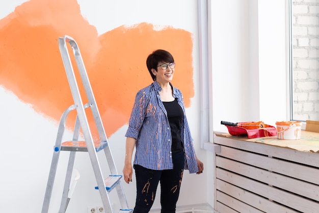 Gelukkige vrouw op middelbare leeftijd schilderen muur in haar nieuwe appartement. Renovatie, herinrichting en reparatie
