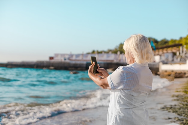 Gelukkige vrouw op vakantie fotograferen met een camera op het strand van de zee door smartphone, geniet van vrije tijd en zomervakantie