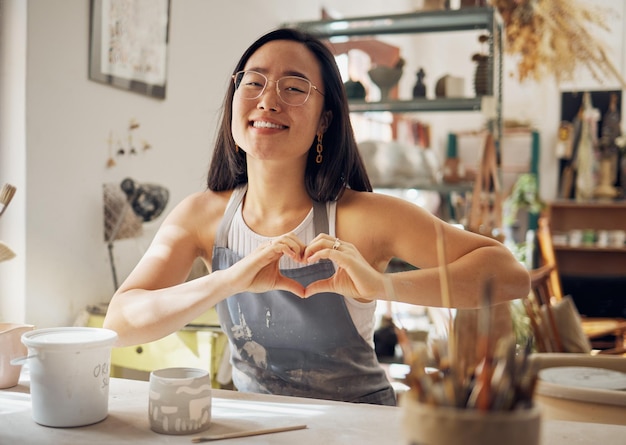 Foto gelukkige vrouw portret of hart handgebaar in aardewerk studio aziatisch klein bedrijf of creatieve keramische workshop glimlach klei of kunst modder werker verliefd ondersteuning of vertrouwen stem van opstarten winkel succes