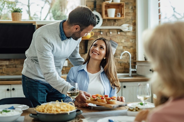 Gelukkige vrouw praat met haar man die eten serveert terwijl ze een familielunch heeft in de eetkamer