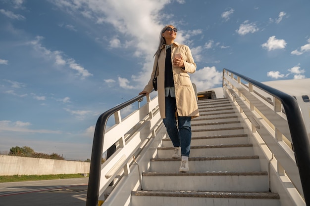 Gelukkige vrouw reiziger in zonnebril naar beneden op de trap van het vliegtuig na de landing op de luchthaven