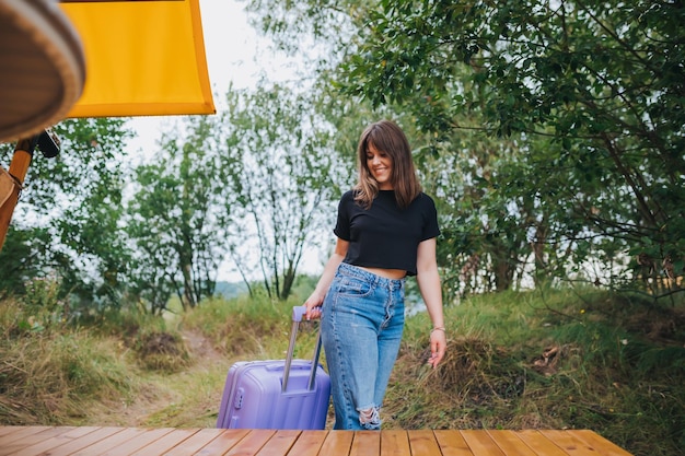 Gelukkige vrouw reiziger met bagage op weg naar slaapkamer van gezellig glamping huis Luxe camping tent voor buiten zomervakantie en vakantie Lifestyle concept