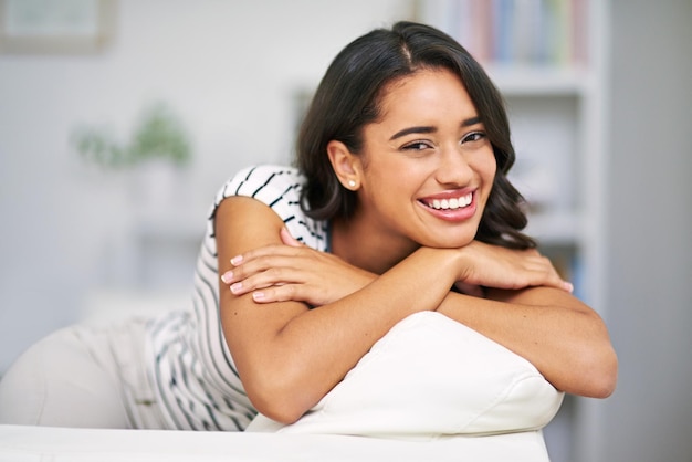 Gelukkige vrouw sofa en glimlach portret in huis om te ontspannen met positieve mindset geluk en vrede van natuurlijke schoonheid Jonge vrouw op bank in de woonkamer in Brazilië huis voor vrije tijd en wellness