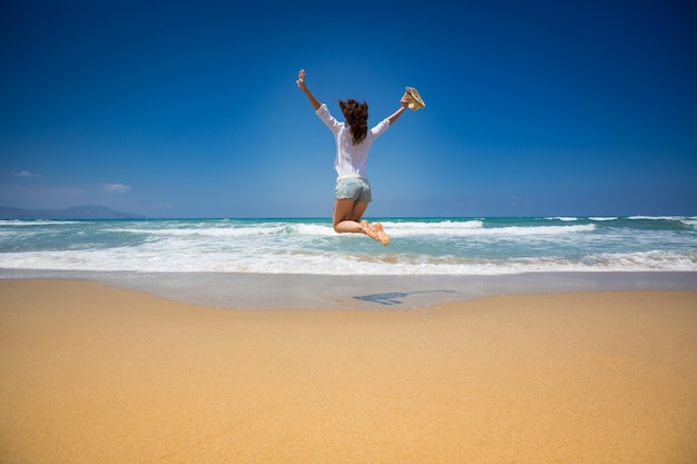 Gelukkige vrouw springen op het strand tegen blauwe lucht en zee Zomervakanties concept