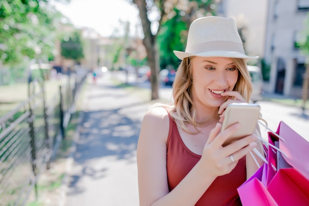 Gelukkige vrouw tekst op haar mobiele telefoon op de straat met kopie ruimte