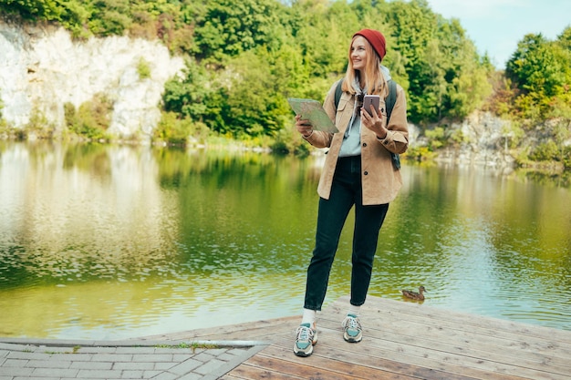 Gelukkige vrouw toerist met rugzak en rode hoed met papieren kaart wandelen in bergen met uitzicht op het meer achtergrond Reis- en reislustconcept Verbazingwekkend chill moment