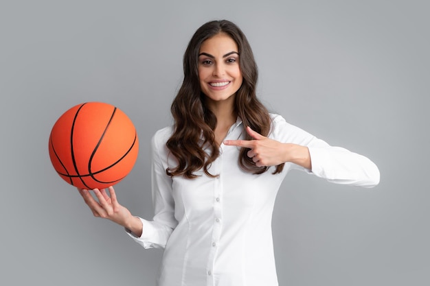 Gelukkige vrouw wijzende vinger op basketbal bal geïsoleerd op een grijze achtergrond