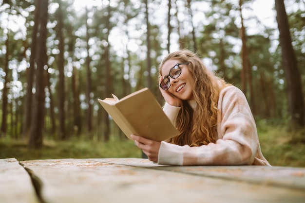 Gelukkige vrouw zit aan tafel met een boek in een prachtig bos Concept van ontspanning levensstijl