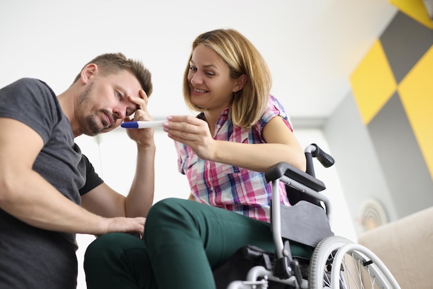 Foto gelukkige vrouw zit in een rolstoel en laat haar man positieve zwangerschapstest zien