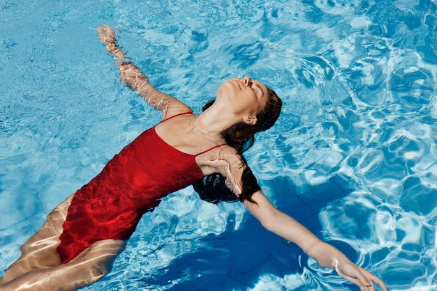 Gelukkige vrouw zwemt in het zwembad in rood badpak met losse lange haren huidbescherming met zonnebrandcrème