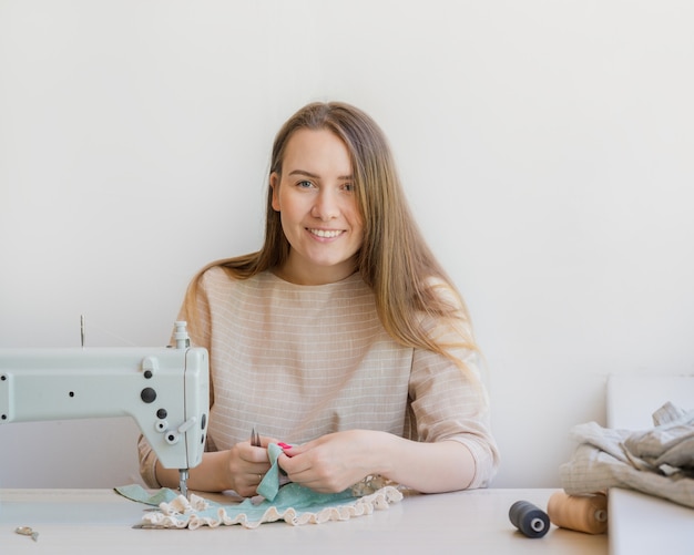 Gelukkige vrouwelijke ateliereigenaar die op de werkplek werkt met een naaimachine