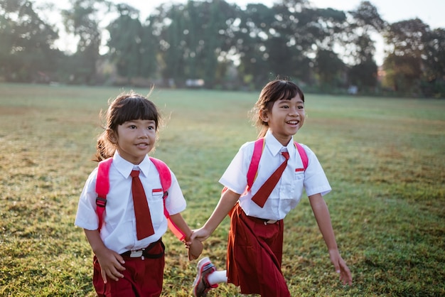 Gelukkige vrouwelijke Aziatische basisschoolleerlingen lopen samen