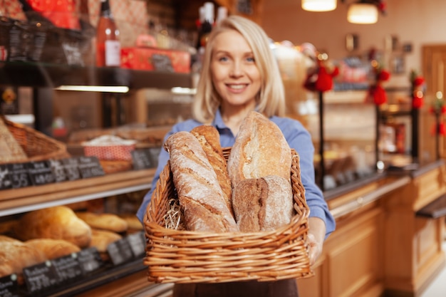 Gelukkige vrouwelijke bakker die bij haar bakehouse werkt, brood in een mand stak