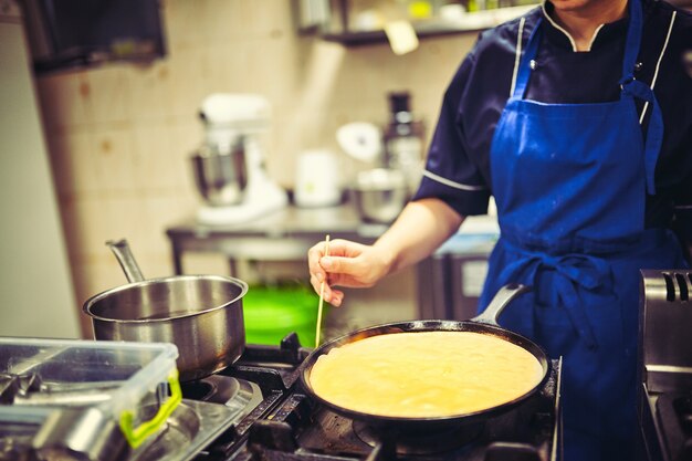 Gelukkige vrouwelijke chef-kok die voedsel kookt in de keuken van het restaurant