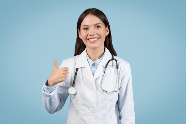 Gelukkige vrouwelijke dokter in witte jas met duimen omhoog.