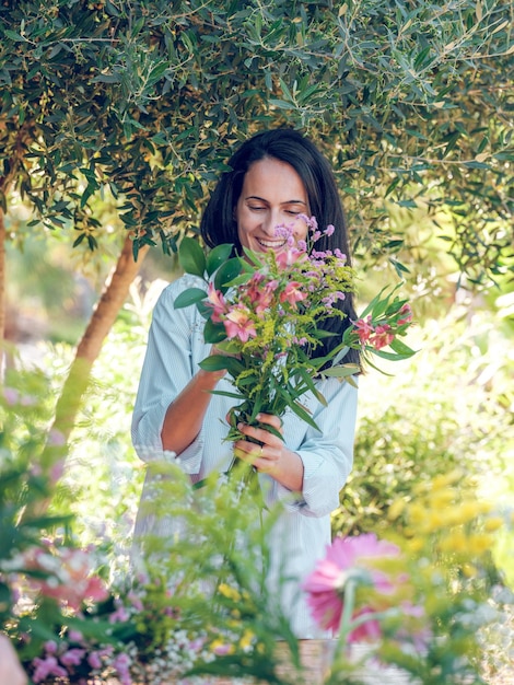 Gelukkige vrouwelijke meester overweegt een boeket bloemen in handen terwijl hij in de tuin staat in de zomer