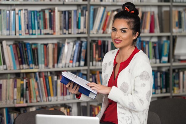 Gelukkige vrouwelijke student die met laptop in bibliotheek werkt