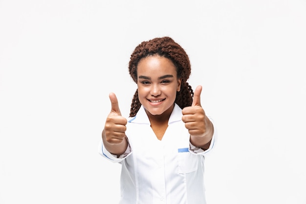 gelukkige vrouwelijke verpleegster glimlachend en duimen opdagen geïsoleerd tegen een witte muur