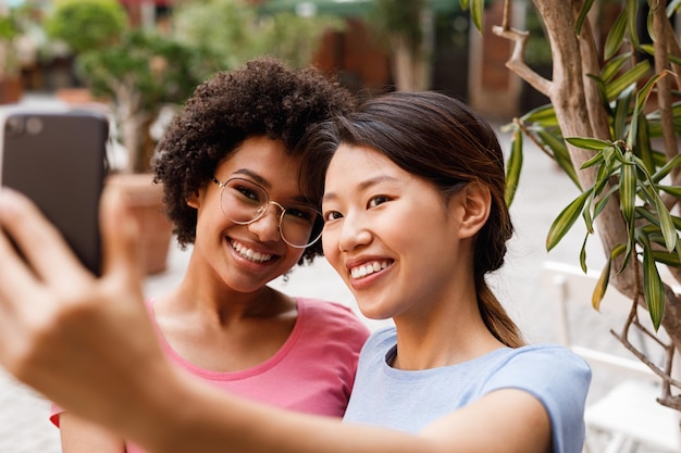 Gelukkige vrouwelijke vrienden die een selfie maken terwijl ze buiten zitten