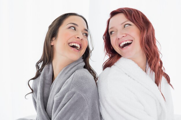 Gelukkige vrouwelijke vrienden in badjassen die zich rijtjes bevinden