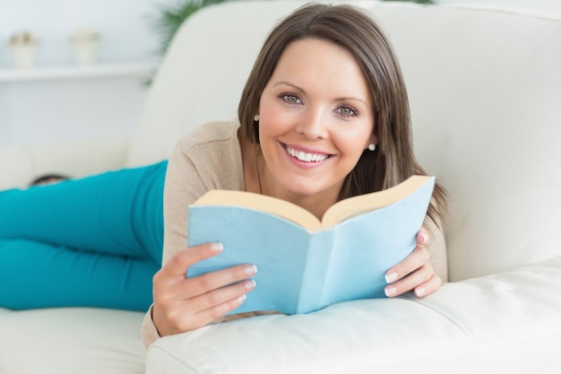 Gelukkige vrouwen die een boek lezen en op de bank liggen