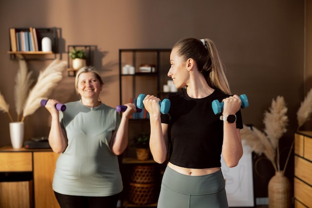 Gelukkige vrouwen die kleding dragen om te trainen, doen oefeningen met halters die naar elkaar kijken