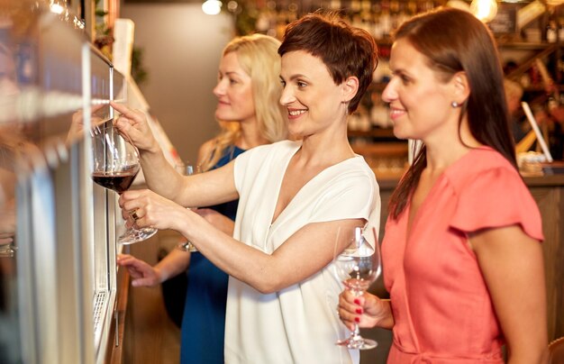 Gelukkige vrouwen die wijn uit de dispenser bij de bar gieten.