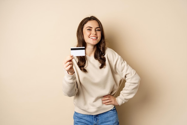 Gelukkige vrouwenklant die creditcard toont die tevreden glimlacht die zich over beige achtergrond bevindt
