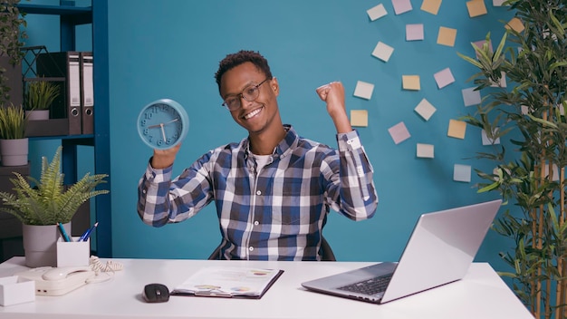 Gelukkige werknemer die de tijd op de klok controleert en het werk vóór de deadline afrondt, aftellend voor time-out. Punctuele man voelt zich vrolijk over de timing van de pauze, kijkend naar horloge met uur en minuten.