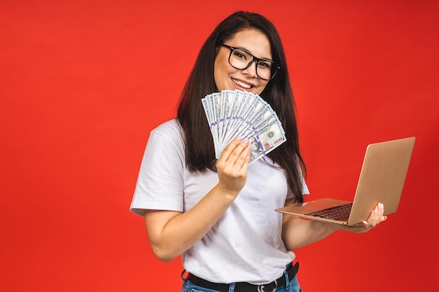 Gelukkige winnaar mooie jonge zakenvrouw in casual bedrijf laptop op kantoor geïsoleerd op rode achtergrond werken met computer met geldrekeningen