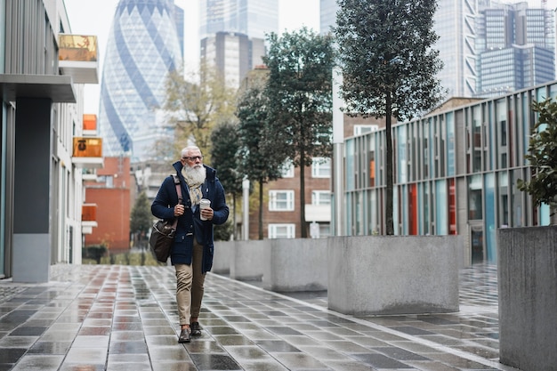 Gelukkige zakelijke senior man loopt naar zijn werk op een regenachtige herfstdag - Focus face