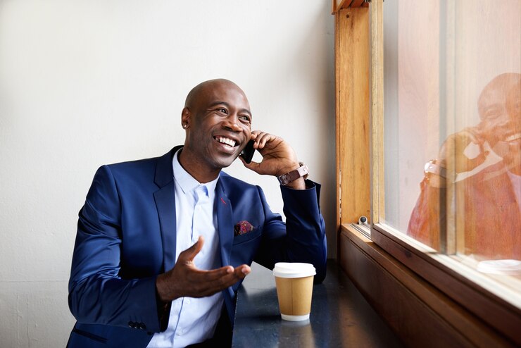 Gelukkige zakenman bij een koffie die op celtelefoon spreekt