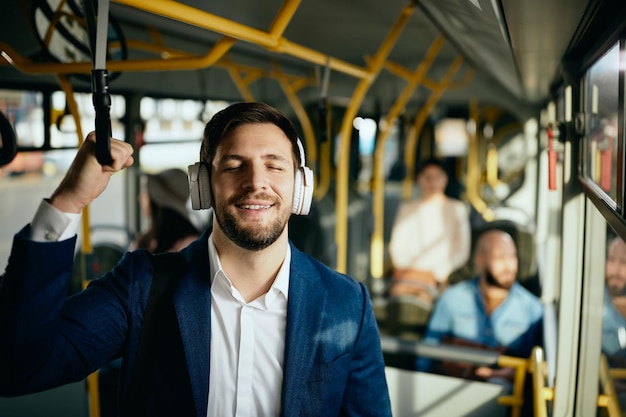 Gelukkige zakenman die muziek luistert via een koptelefoon tijdens het woon-werkverkeer met de bus