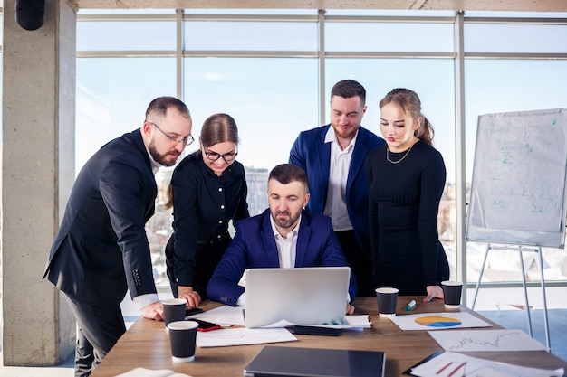 Gelukkige zakenmensen kijken naar laptoppresentatie, succes op het werk, zittend in een modern kantoor. Succesvolle online onderhandelingen. Ondernemers delen hun kennis