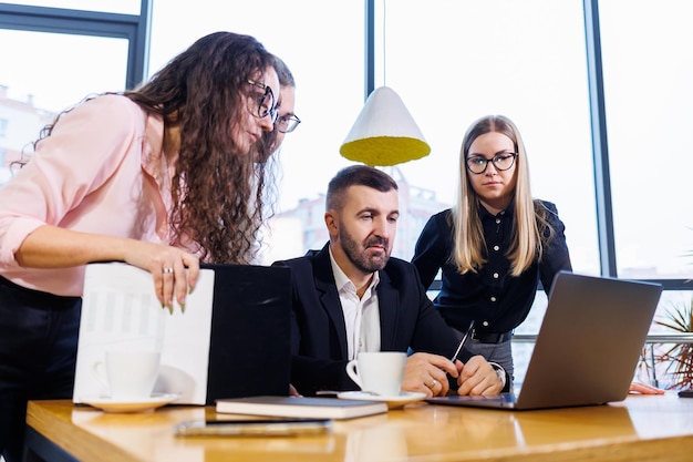 Gelukkige zakenmensen kijken naar laptoppresentatie, succes op het werk, zittend in een modern kantoor. Succesvolle online onderhandelingen. Ondernemers delen hun kennis