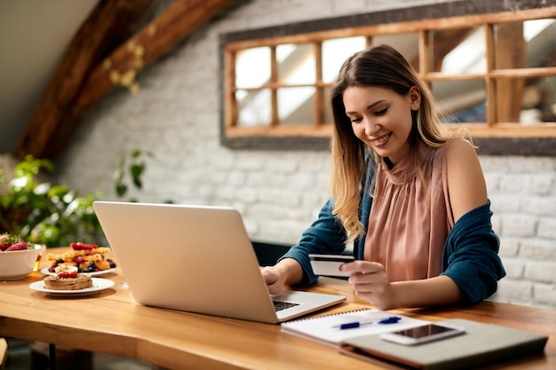 Gelukkige zakenvrouw die laptop en creditcard gebruikt terwijl ze thuis aan het e-bankieren is