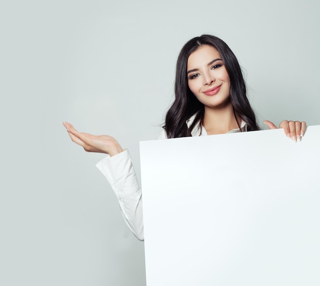 Gelukkige zakenvrouw die lege open hand toont en witte blanco papier banner achtergrond vasthoudt Jonge vrouw die lacht bedrijfs- en onderwijsconcept