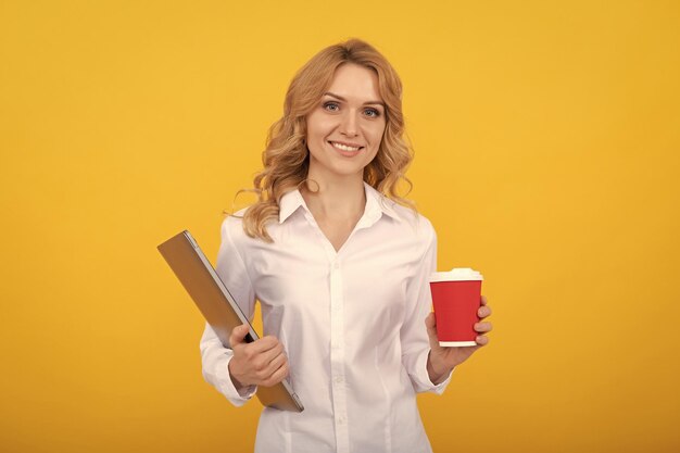 Gelukkige zakenvrouw met laptop houdt afhaalmaaltijden papieren beker gele achtergrond koffiedrankje