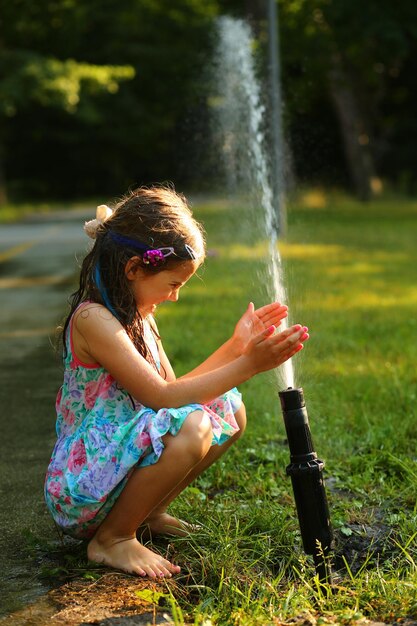 Gelukkige zesjarig meisje speelt met een watersprinkler in het zonnige park in de zomer