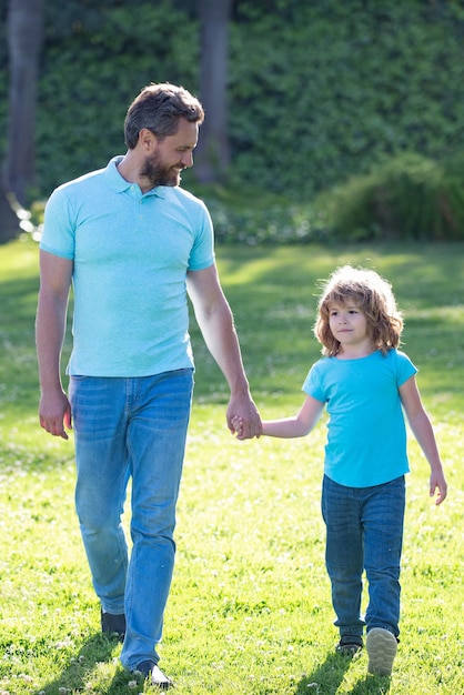 Gelukkige zoon en vader hand in hand lopen op zonnige zomerdag in park gras, saamhorigheid.