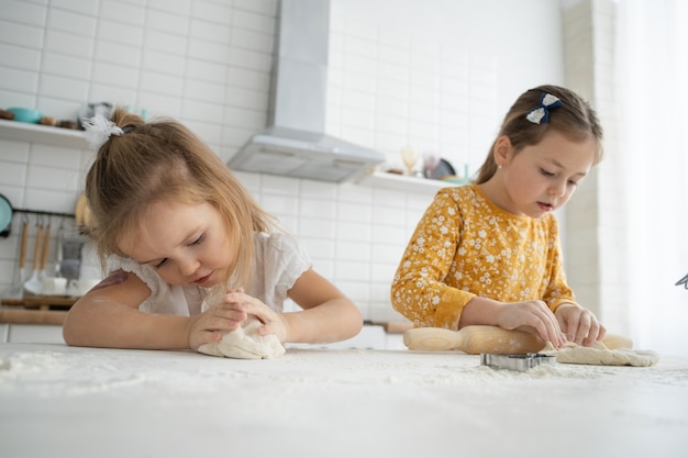 Gelukkige zussen kinderen meisjes bakken koekjes, kneed deeg, spelen met bloem en lachen in de keuken.