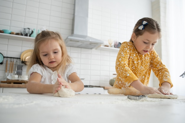 Gelukkige zussen kinderen meisjes bakken koekjes, kneed deeg, spelen met bloem en lachen in de keuken.