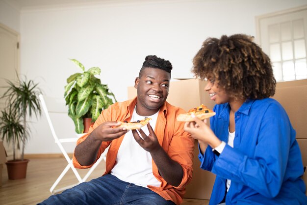 Gelukkige zwarte echtgenoten die pizza eten en plezier hebben op de verhuisdag