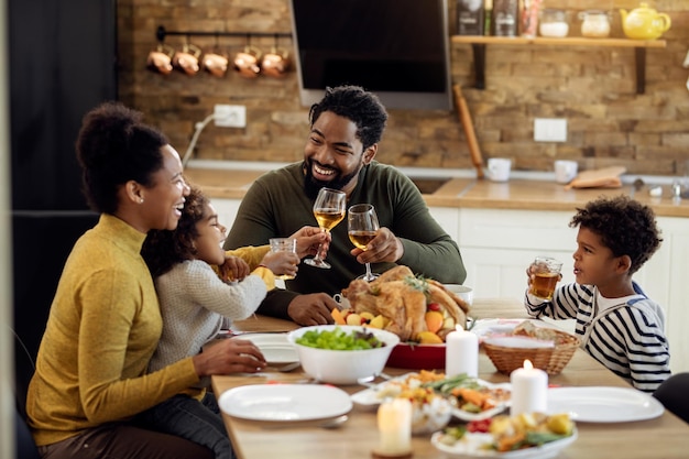 Gelukkige zwarte familie roosteren tijdens Thanksgiving-lunch in de eetkamer