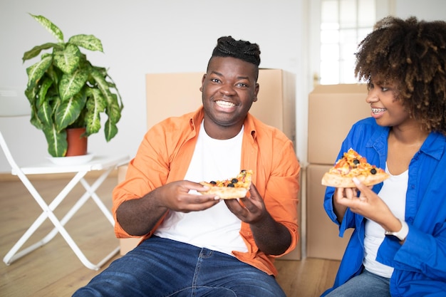 Gelukkige zwarte man en vrouw die pizza eten en de verhuisdag vieren