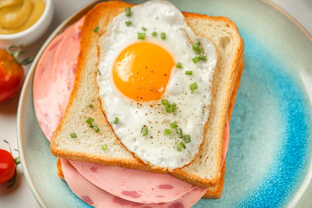 Gemakkelijk ontbijt Close-up - gebakken ei op sandwich met worst op plaat met tomaten, mosterd, ham, toast. Witte achtergrond met tafelkleed. Bovenaanzicht.