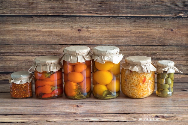 Foto gemarineerde augurken variëteit conservenpotten op de houten keukentafel. gefermenteerde zelfgemaakte gerechten.