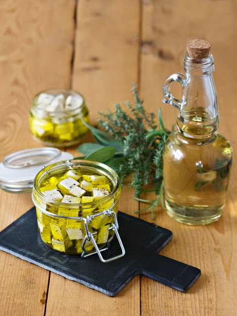 Gemarineerde feta in een glazen pot, specerijen en olijfolie op een houten achtergrond