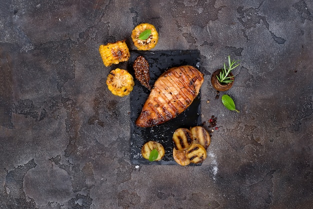 Gemarineerde gegrilde gezonde kipfilets en geserveerd met verse kruiden, aardappelen en maïs