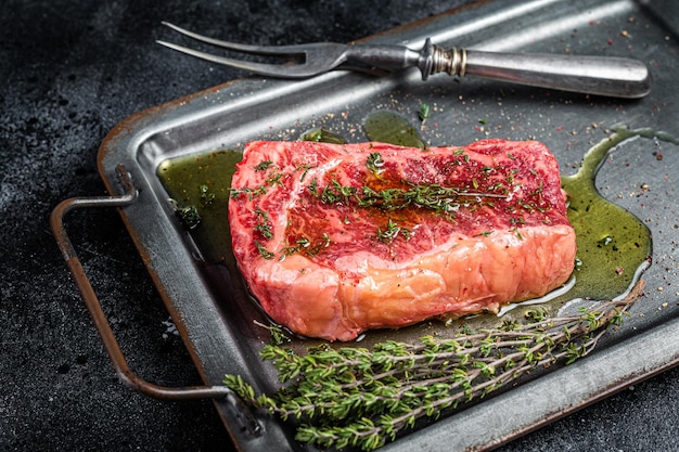 Gemarineerde rauwe striploin New York steak met olijfolie, tijm en peper Zwarte achtergrond Bovenaanzicht